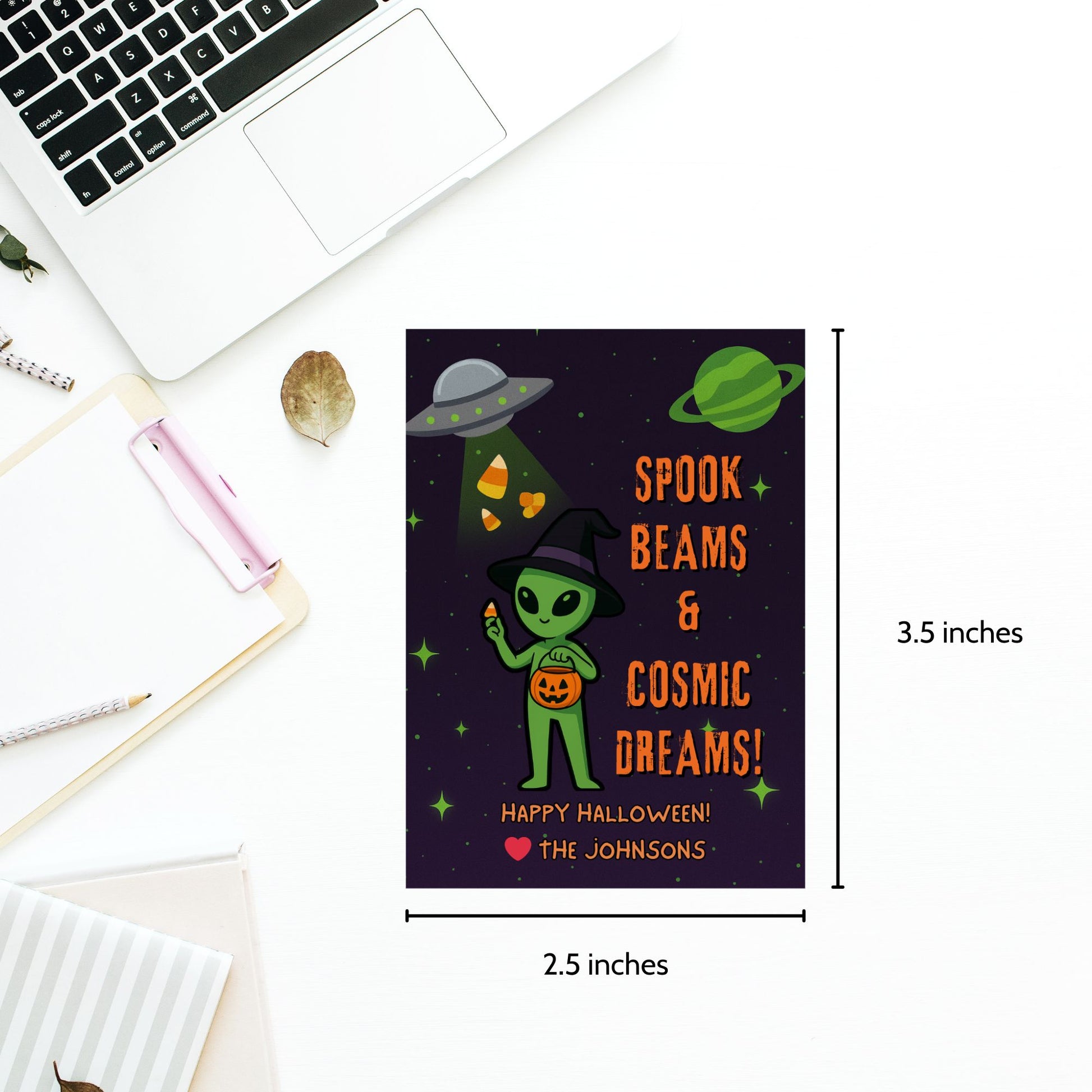 Halloween-themed card with alien design and text, placed on a desk with a laptop.