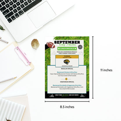 A September lunch menu flyer template displayed on a grassy football field background, surrounded by a laptop, notebook, and pens on a white desk. The flyer includes dimensions of 11 inches by 8.