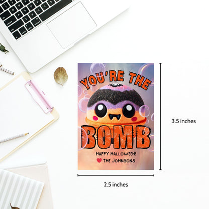 Halloween-themed printable gift tags with the message "You're the Bomb" featuring a cute and spooky bath bomb character, perfect for bath bomb gifts. Tags are 2.5 x 3.5 inches, laid out 8 per sheet on a standard 8.5 x 11-inch page. Includes a printable PDF and a PDF with a link to an editable Canva template.