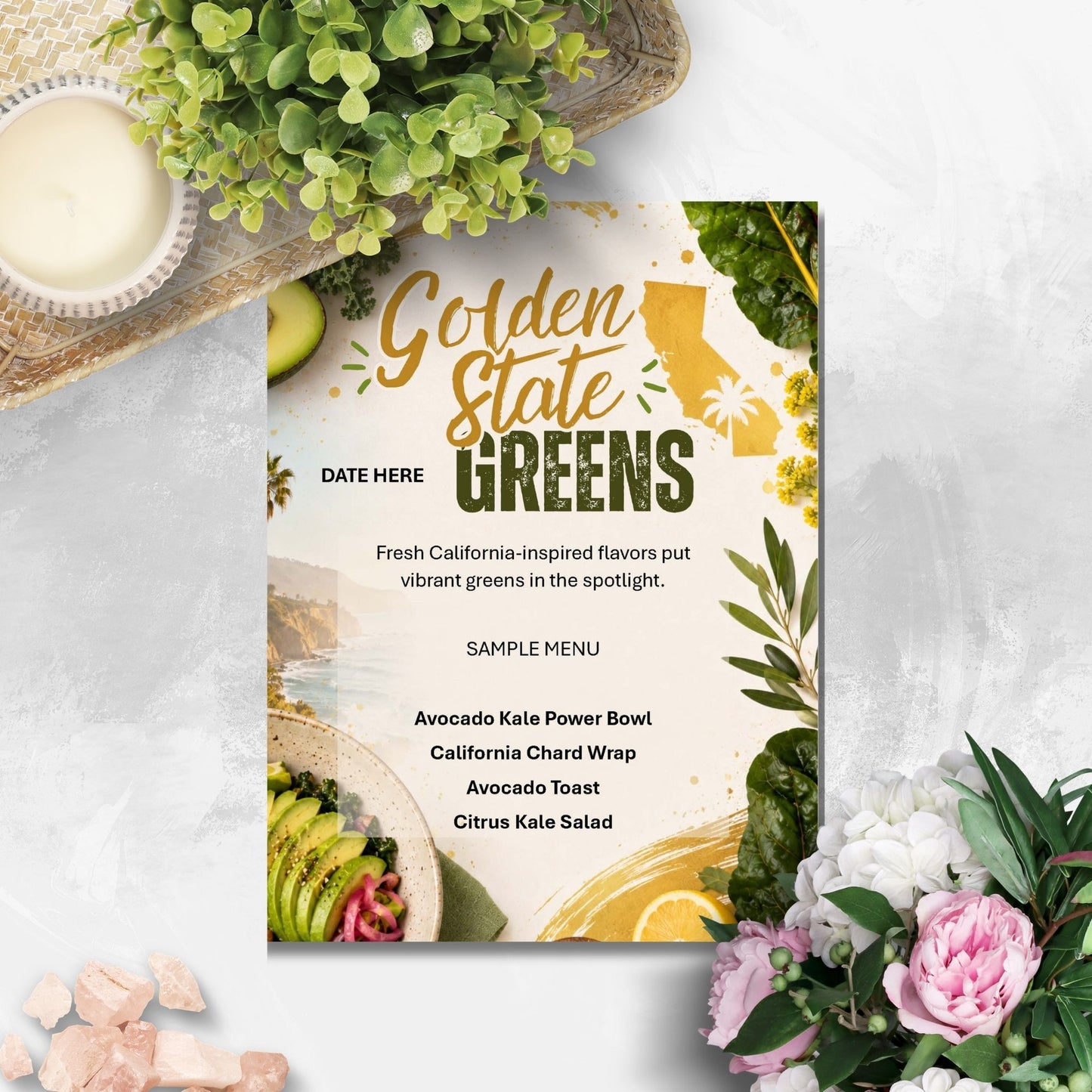 A printed restaurant menu card titled 'Golden State Greens' with green and gold typography, California map graphics, and food photos, styled on a light textured surface with flowers, greenery, and a candle around it.