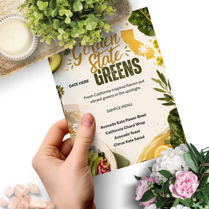 A hand holds a printed menu card for 'Golden State Greens' over a white background, surrounded by green plants, pink flowers, and small stones. The menu features a California-inspired salad theme with text and food illustrations.
