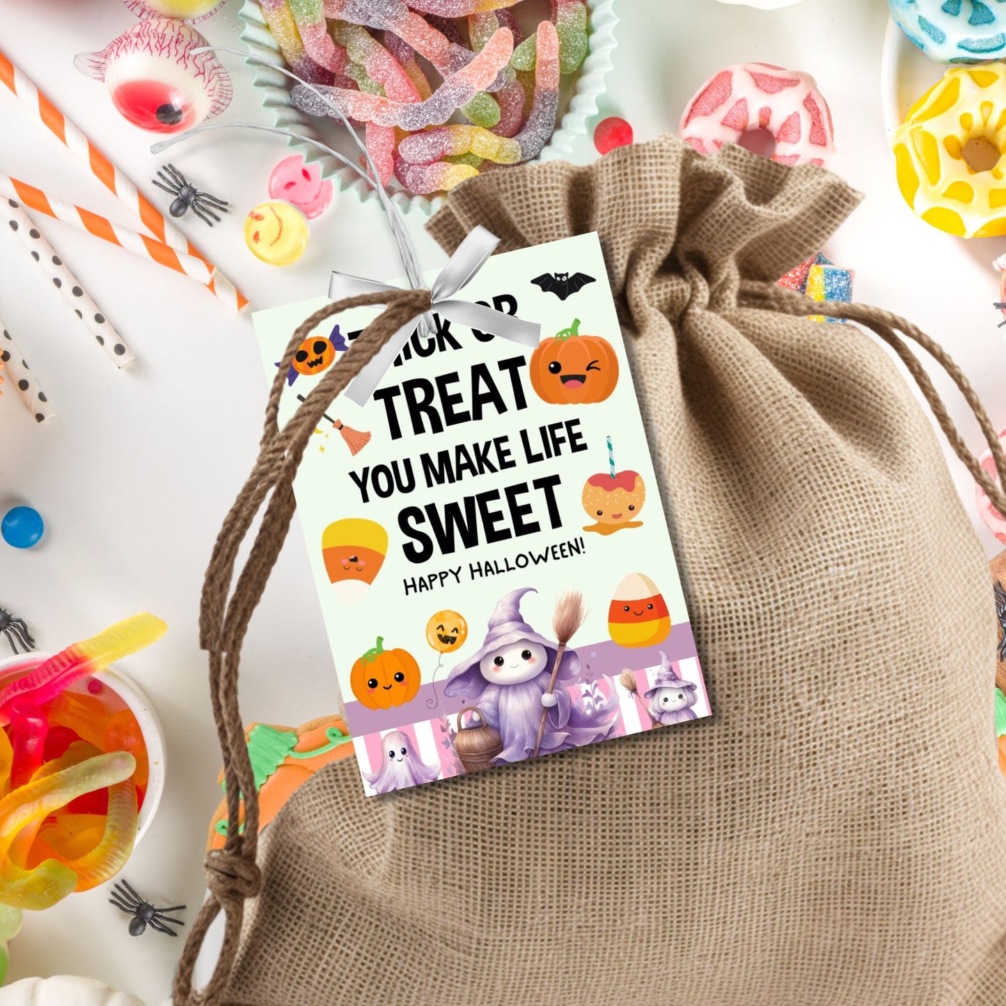 Halloween-themed printable gift tags with the message "Trick or Treat You Make Life Sweet" featuring cute pumpkins, candy corn, and a friendly witch, perfect for trick-or-treat bag gifts. Tags are 2.5 x 3.5 inches, laid out 8 per sheet on a standard 8.5 x 11-inch page. Includes a printable PDF and a PDF with a link to an editable Canva template.