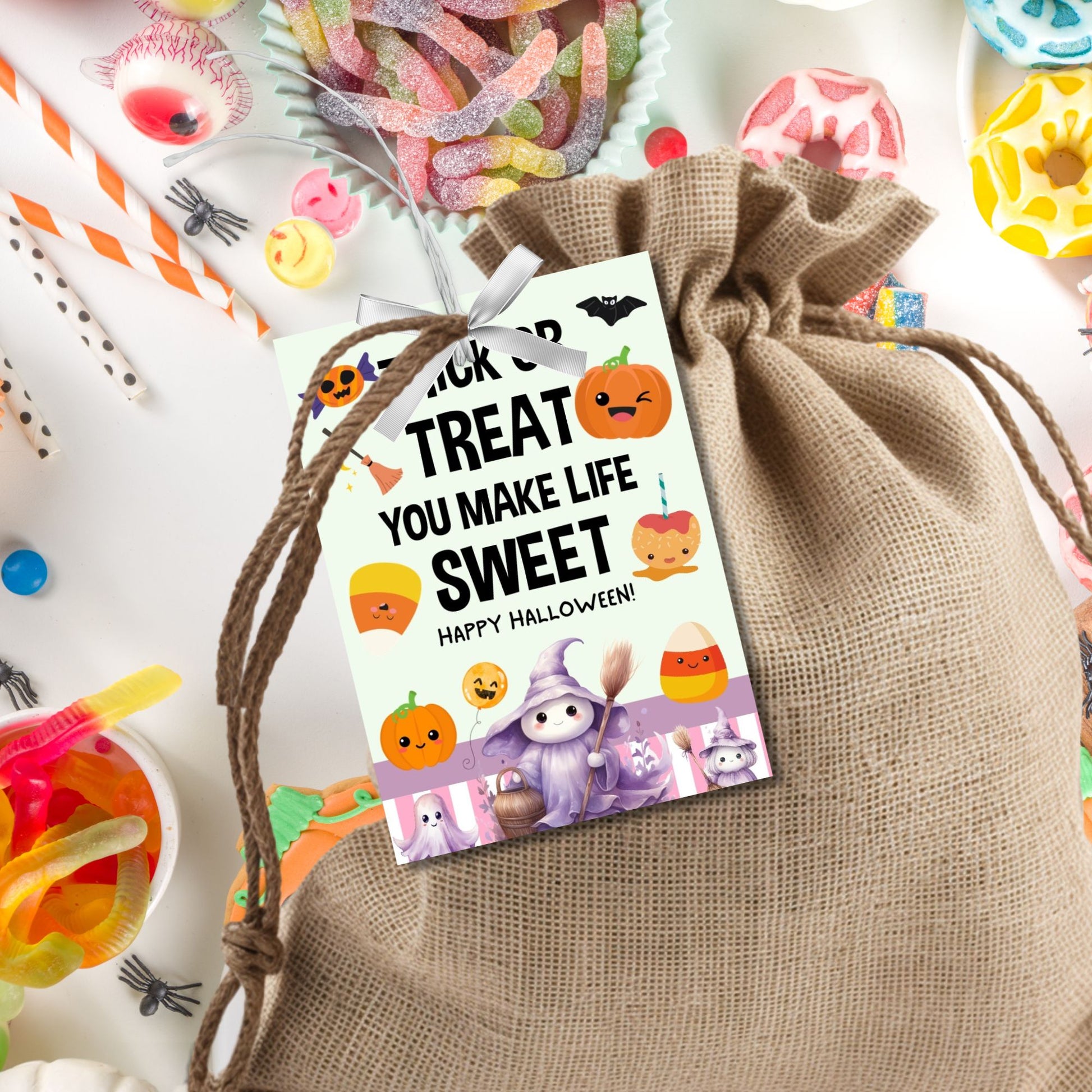Halloween-themed printable gift tags with the message "Trick or Treat You Make Life Sweet" featuring cute pumpkins, candy corn, and a friendly witch, perfect for trick-or-treat bag gifts. Tags are 2.5 x 3.5 inches, laid out 8 per sheet on a standard 8.5 x 11-inch page. Includes a printable PDF and a PDF with a link to an editable Canva template.