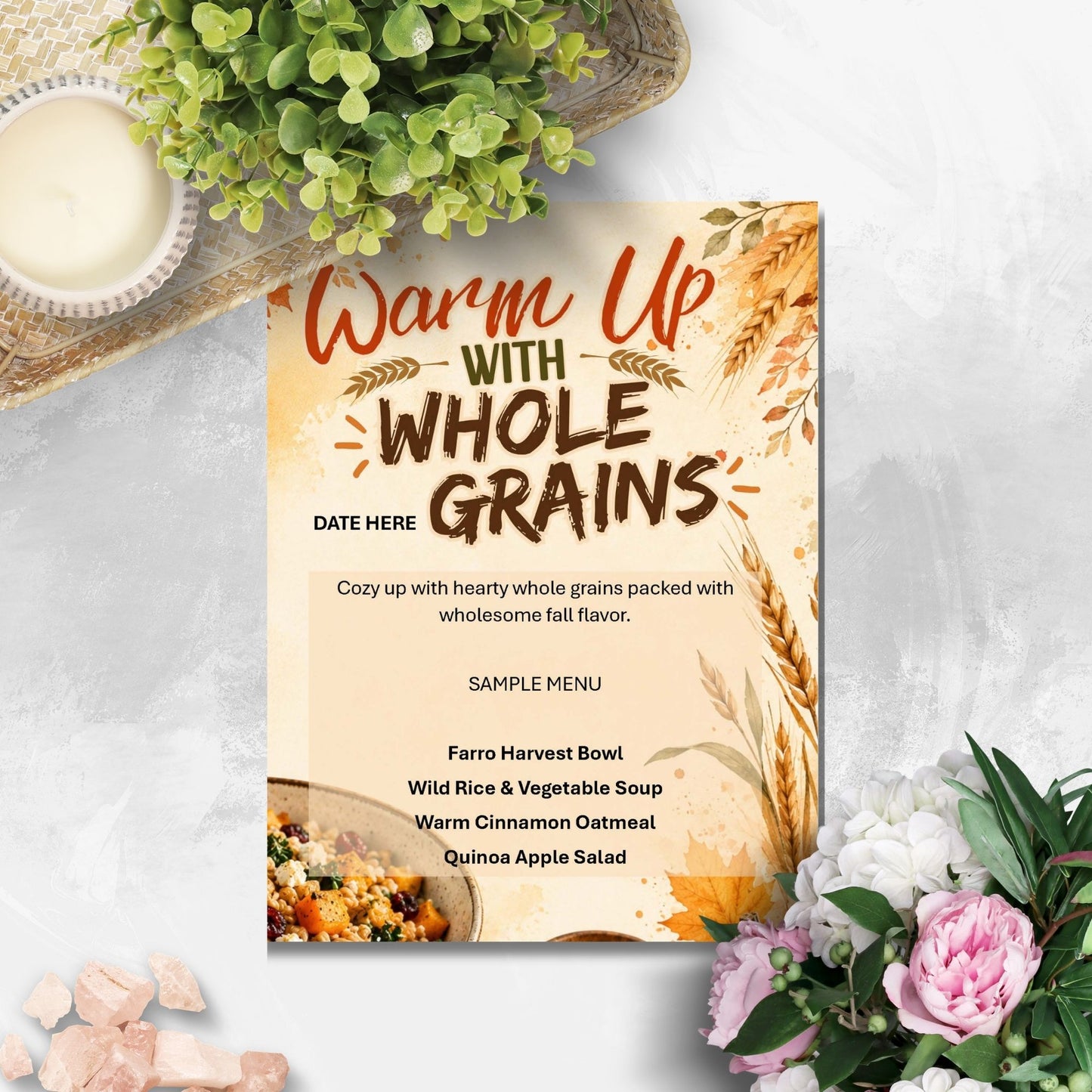 A fall-themed menu card reading 'Warm Up with Whole Grains' styled on a light marble surface with flowers, greenery, and a candle around it.
