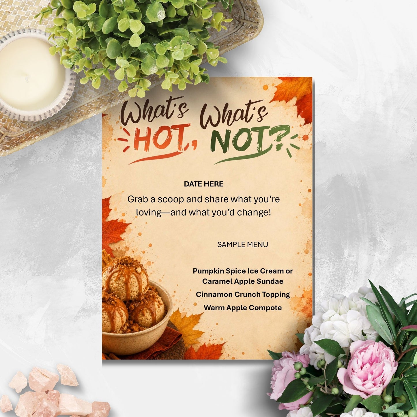 A printed sign or menu card with autumn-themed text reading “What’s HOT, What’s NOT?” and a sample menu, styled on a light surface with flowers, a candle, and greenery around it.